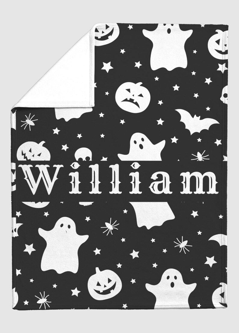 May include: A black and white Halloween-themed blanket featuring a pattern of ghosts, jack-o'-lanterns, stars, and spiders. The name "William" is prominently displayed in white. The blanket is folded, revealing a white underside.