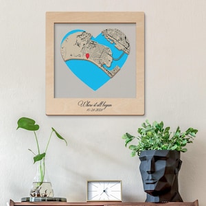 May include: A framed wooden map art piece with a heart-shaped design and a blue backdrop. The map shows a city layout with a red marker. The text "Where it all began" and the date "10-24-2024" are written below the map.