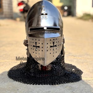 May include: A polished metal knight's helmet with a visor featuring cross cutouts. The helmet is connected to a chainmail coif. The text "Meta Empire" is visible on the lower left side of the image.