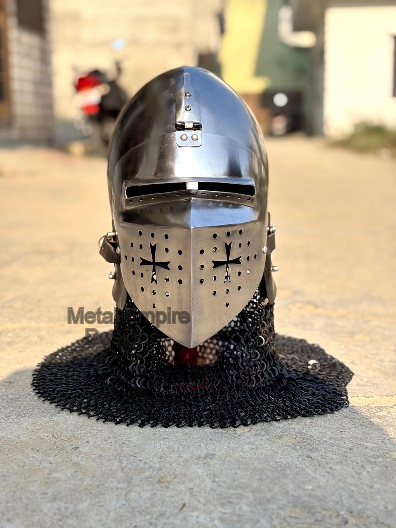May include: A polished metal knight's helmet with a visor featuring cross cutouts. The helmet is connected to a chainmail coif. The text "Meta Empire" is visible on the lower left side of the image.