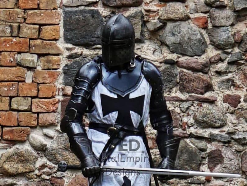 May include: A medieval knight in full black and silver armor, including a helmet, chest plate with a black cross, and gauntlets. The knight holds a sword. The background is a brick and stone wall. The image has the text "ED Metal Empire Designs".