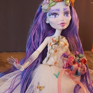 May include: A handcrafted doll with a pale face, purple hair, and a floral crown. The doll wears a white dress with butterfly accents and holds a bouquet. The doll's arm has a butterfly attached. The doll's hair is a mix of purple and blue.