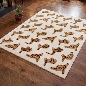 Könnte beinhalten: Rechteckiger Teppich mit cremefarbenem Hintergrund und einem sich wiederholenden Muster aus braunen Leopardenformen. Der Teppich liegt auf einem Holzboden und verleiht der Raumdekoration einen Hauch von Animal-Print.