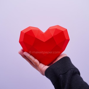 Op de afbeelding: Een felrood, driedimensionaal geometrisch hart van papier met een gefacetteerd low-poly ontwerp. Het oppervlak bevat de tekst makeitpaper.com, gedrukt in kleine witte letters in het midden van de hartvorm.