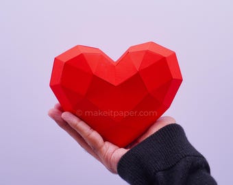 May include: A bright red, three-dimensional geometric heart sculpture made of paper with a faceted, low-poly design. The surface features the text makeitpaper.com printed in small white letters across the center of the heart shape.