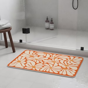 Può includere: Tappetino da bagno rettangolare con un motivo ripetuto di grandi margherite stilizzate. I fiori sono color crema con centri arancioni, su uno sfondo arancione vibrante. Il tappetino è posizionato su un pavimento piastrellato bianco.