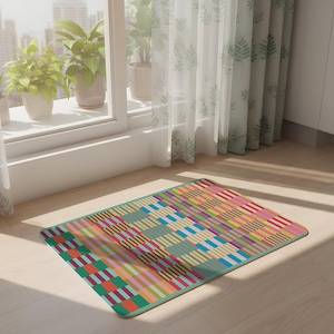 Può includere: Un tappeto rettangolare con un motivo geometrico colorato. Il design presenta strisce e blocchi nei toni del rosso, arancione, giallo, verde, blu e rosa. Il tappeto ha un bordo turchese ed è posizionato su un pavimento in legno chiaro.