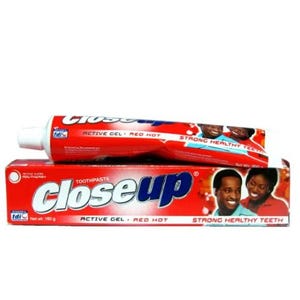 May include: A red and white tube and box of Close Up toothpaste. The tube and box feature the brand name in a blue and white font. The box and tube also have images of people smiling.