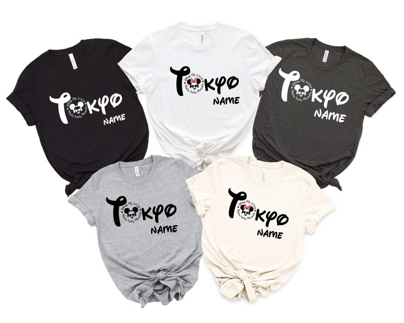 May include: Five short-sleeved t-shirts in black, white, charcoal, gray, and cream. Each shirt features the word "Tokyo" in stylized script, a Mickey Mouse graphic, and the word "NAME" below. The shirts are knotted at the waist.