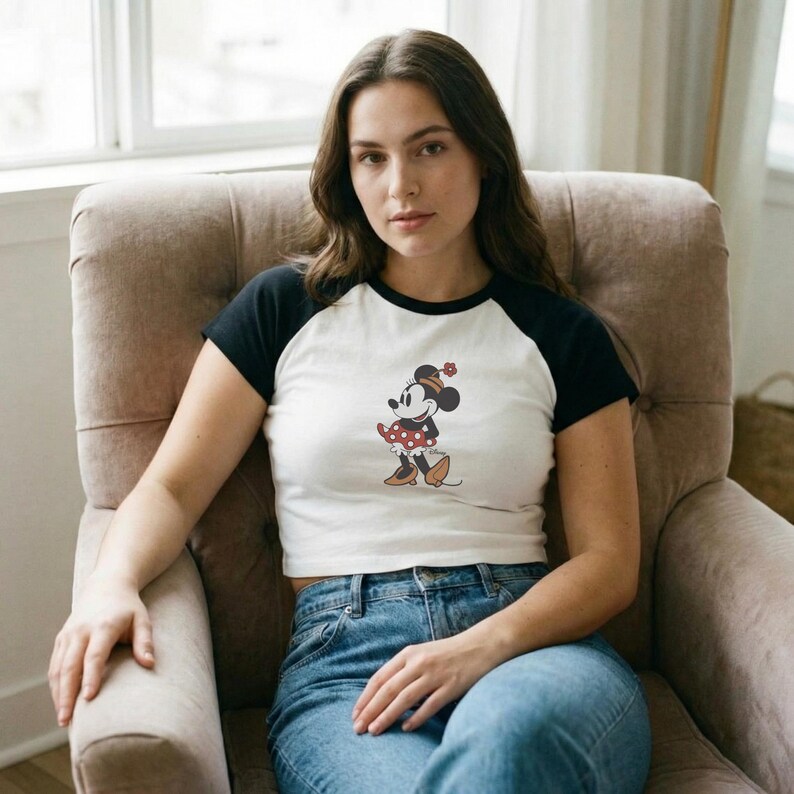 Puede incluir: Un top corto ragl&aacute;n blanco y negro con un gr&aacute;fico de Minnie Mouse. El gr&aacute;fico muestra a Minnie Mouse con un vestido de lunares rojos y un lazo a juego. El top se combina con unos vaqueros azules.