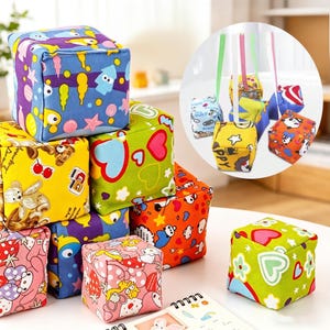 Può includere: Una collezione di cubi di tessuto colorati con vari motivi, tra cui cuori e personaggi dei cartoni animati. Alcuni cubi sono impilati, altri sono appesi con nastri. I cubi sono in tonalità di blu, giallo, verde, arancione e rosa. Misurano circa 10 cm per lato.