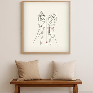 Puede incluir: Una impresión artística enmarcada con un dibujo lineal minimalista de dos manos. Las manos están dibujadas con una sola línea negra continua, con acentos rojos. La obra de arte se muestra sobre un fondo claro, enmarcada en un marco de madera natural.