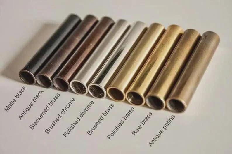 May include: A collection of metal tubes in various finishes, including matte black, antique black, and brushed brass. The image displays a range of colors from dark to light, with text labels identifying each finish. The tubes are arranged in a row, showcasing their different appearances.