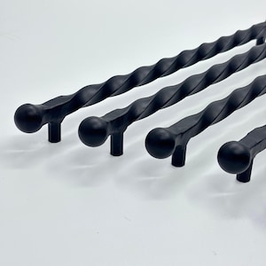 May include: Four black, twisted metal cabinet pulls with a matte finish. Each pull has a rounded end and a cylindrical base. The pulls are arranged diagonally, showcasing their decorative, textured design. Ideal for adding a touch of elegance to furniture.