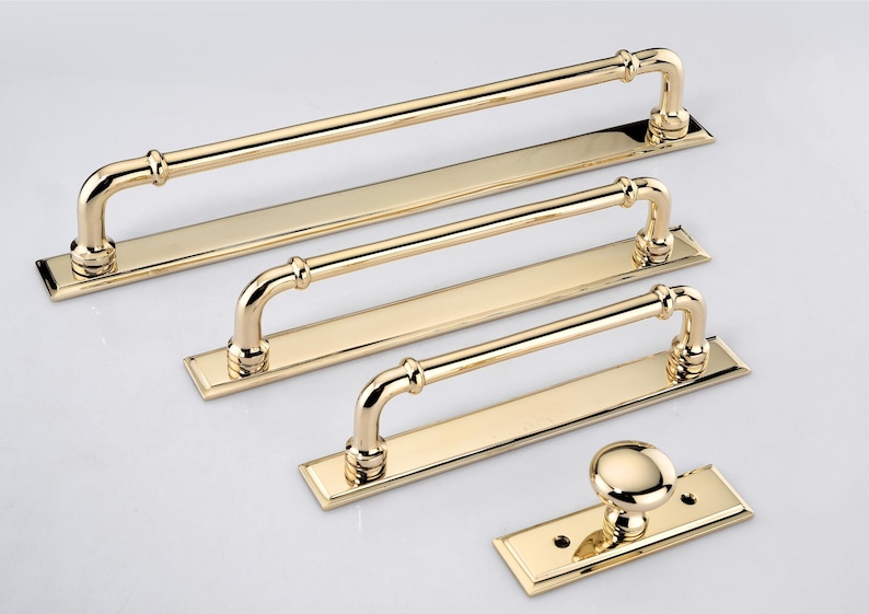 May include: A collection of polished gold-tone hardware including three rectangular cabinet pulls with arched handles and one matching round cabinet knob, each mounted on a flat rectangular base plate with visible screw holes at the ends.