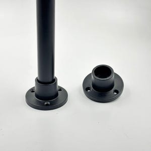 May include: Two black metal pipe flanges and a black metal pipe. The flanges are round with three holes for mounting. The pipe is cylindrical and appears to be a support or structural element.