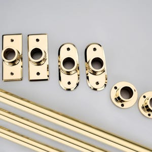 May include: A set of polished gold-tone metal hardware including three long cylindrical rods and six mounting brackets in three distinct shapes: two rectangular, two oval, and two circular, each featuring central openings and screw holes.