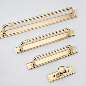 May include: A set of four polished gold-tone metal hardware pieces consisting of three rectangular cabinet pulls with arched handles and one single round cabinet knob, each mounted on a matching rectangular base plate with visible screw holes.