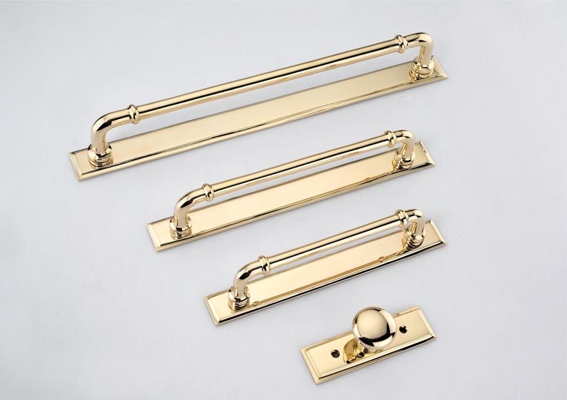 May include: A set of four polished gold-tone metal hardware pieces consisting of three rectangular cabinet pulls with arched handles and one single round cabinet knob, each mounted on a matching rectangular base plate with visible screw holes.