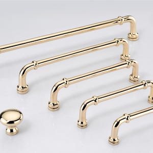 May include: A collection of polished gold-toned cabinet hardware, including one round knob and five arched bar pulls of varying lengths. Each piece features a smooth, reflective metallic finish with cylindrical bars and circular mounting bases.