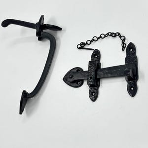 May include: Black wrought iron gate latch and handle set. The set includes a curved handle with a decorative backplate and a latch with a chain. The latch has a decorative heart-shaped backplate. The hardware is designed for outdoor use.