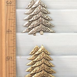 May include: Two metal Christmas tree ornaments, one silver and one gold, with a textured surface. The ornaments are about 2 inches tall and are shown against a white wooden background.