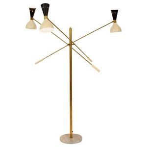 Op de afbeelding: Een moderne vloerlamp uit het midden van de eeuw met een messingkleurige paal en een ronde marmeren voet. De lamp heeft drie off-white conische tinten met zwarte en messing accenten, en vier kleinere witte en messing accenten.