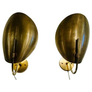 May include: Two brass wall sconces with an organic, teardrop-shaped design. Each sconce features a curved, golden shade and a circular base. The sconces have a mid-century modern aesthetic, with a sleek and minimalist design.