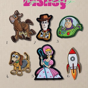 Può includere: Toppe Disney Toy Story ricamate con personaggi come Woody, Buzz Lightyear e Bo Peep. Le toppe sono numerate da 1 a 6. Il logo Disney è in alto. Il testo in basso dice: "Inserisci il numero della toppa che desideri acquistare nella casella di personalizzazione. (Patch Free Size)"