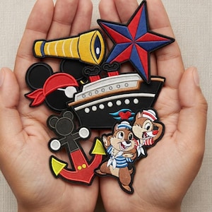 May include: A collection of embroidered patches featuring nautical and cartoon themes. Includes a red and blue star, a black ship, a yellow telescope, a Mickey Mouse pirate, a red and yellow anchor, and Chip and Dale characters.
