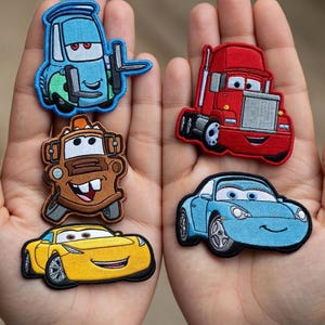 Könnte beinhalten: Gestickte Aufnäher mit Zeichentrickfiguren von Autos in Blau, Rot, Braun, Gelb und Hellblau. Die Aufnäher haben detaillierte Stickereien und lächelnde Gesichter in verschiedenen Formen und Größen.
