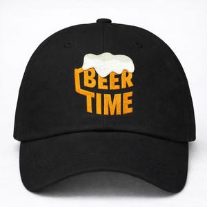 Könnte beinhalten: Schwarze Baseballkappe mit einem gestickten Design. Das Design zeigt die Worte "BEER TIME" in Orange, mit einer weißen Schaumgrafik über dem Text, die einen Bierkrug andeutet. Die Kappe hat einen gebogenen Schirm und einen Knopf oben.