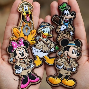 Puede incluir: Parches bordados con los personajes de Disney Pluto, Goofy, Pato Donald, Mickey Mouse y Minnie Mouse con trajes de safari. Cada parche tiene un diseño detallado con colores vibrantes y un borde marrón. Perfecto para añadir a ropa o accesorios.