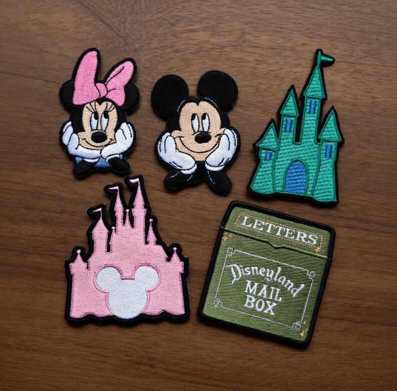 May include: Embroidered patches featuring Mickey Mouse, Minnie Mouse, and two castle designs. One patch is a green castle, and the other is pink. A green patch reads "Disneyland Mail Box" and "Letters".