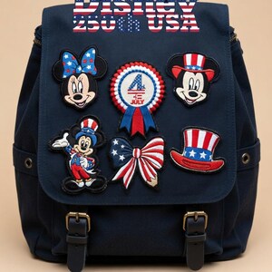 May include: A navy blue backpack adorned with embroidered patches featuring Disney characters and patriotic symbols. Patches include Minnie and Mickey Mouse, a bow, a top hat, and a 4th of July ribbon. The text "Disney 250th USA" is at the top.