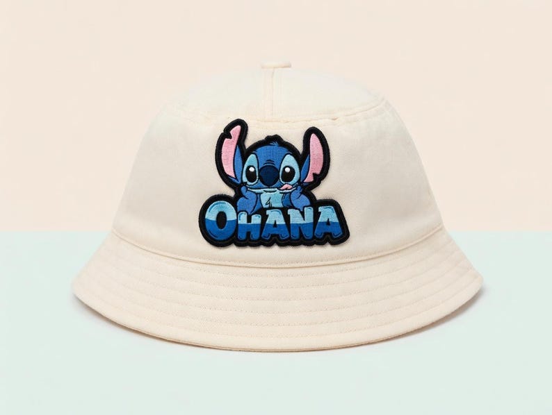 May include: Cream-colored bucket hat featuring a blue and black patch of the character Stitch with the word "OHANA" in blue lettering. The hat has a rounded crown and a downward-sloping brim, suitable for sun protection.