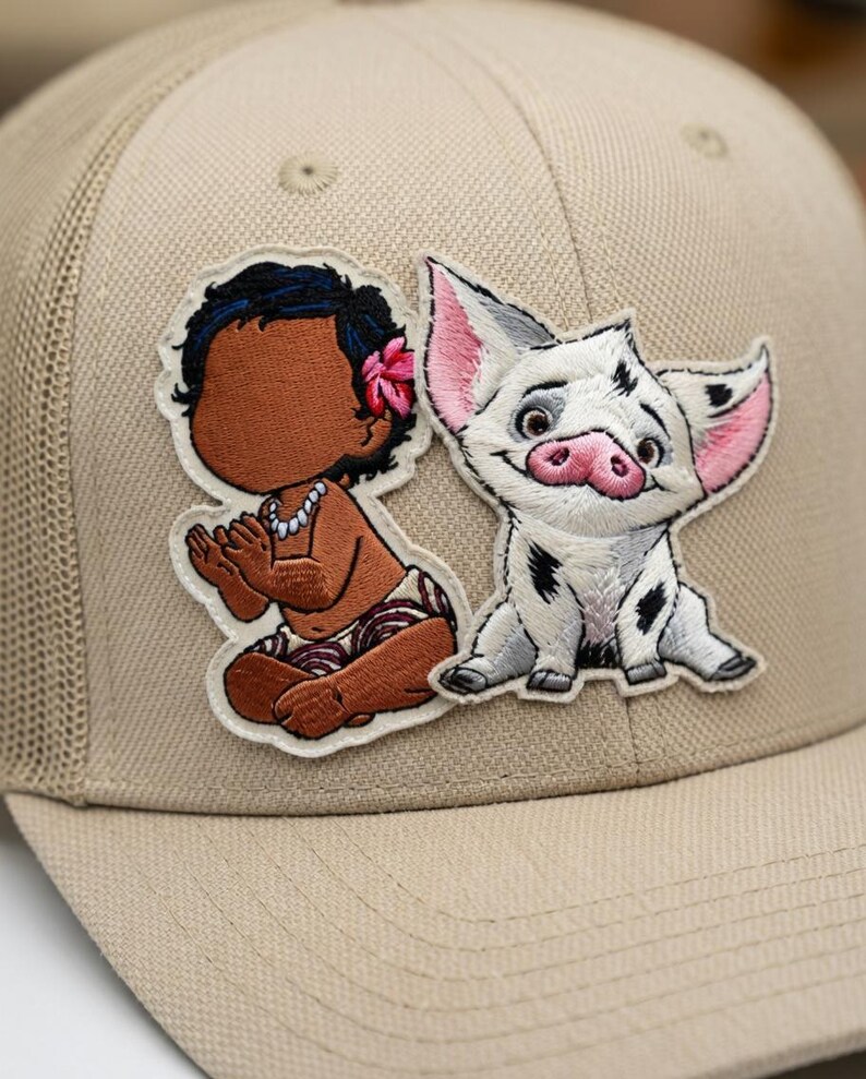 May include: Tan trucker hat featuring embroidered patches of a cartoon baby and a pig. The baby has brown skin, black hair, and a pink flower. The pig is white with black spots and pink ears and snout.