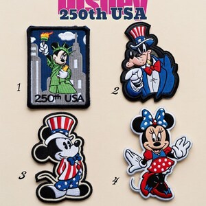 Könnte beinhalten: Vier Disney-Themen-Stickpatches. Patch 1 zeigt Micky Maus als Freiheitsstatue. Patch 2 zeigt Goofy in einem patriotischen Outfit. Patch 3 zeigt Micky Maus in einem rot-weiß-blauen Outfit. Patch 4 ist Minnie Maus in einem rot-weiß gepunkteten Kleid.
