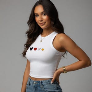 May include: White ribbed crop top with a crew neck and a colourful Mickey Mouse graphic. The graphic features Mickey's head, gloves, and shoes. The top is paired with blue jeans.