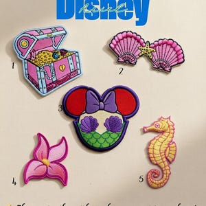 May include: Embroidered patches featuring Disney's Ariel theme. Designs include a pink treasure chest, pink seashells with a starfish, a Minnie Mouse-inspired design, a pink flower, and a yellow seahorse. The word "Disney" is written in blue.
