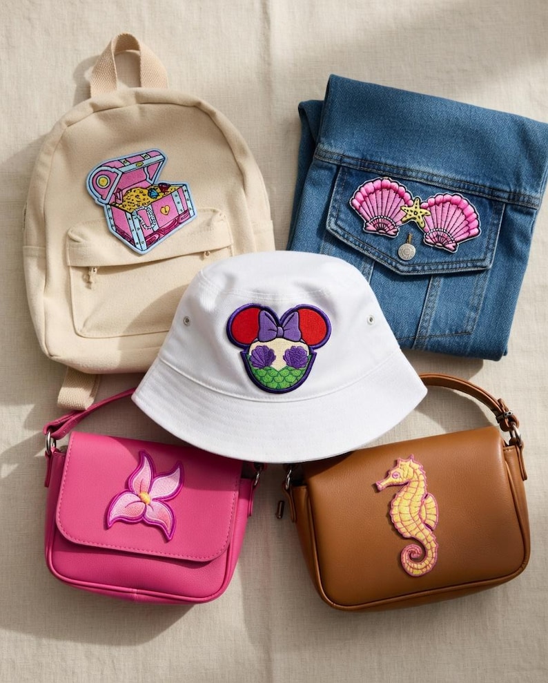 May include: An assortment of accessories featuring embroidered patches. Includes a beige backpack with a treasure chest, a denim jacket with seashell patches, a white bucket hat with a Minnie Mouse design, a pink purse with a flower, and a brown purse with a seahorse.