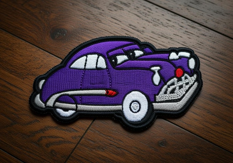 May include: Embroidered patch of a purple cartoon car with white accents, black outline, and a red detail. The car has a smiling face and white wheels. The patch is on a wooden surface.