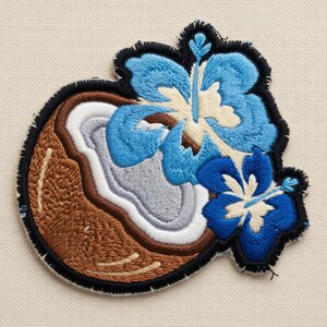 May include: Embroidered patch featuring a coconut and two blue hibiscus flowers. The coconut is brown with white and gray details, outlined in black. The flowers have blue petals and white centers, with black outlines.