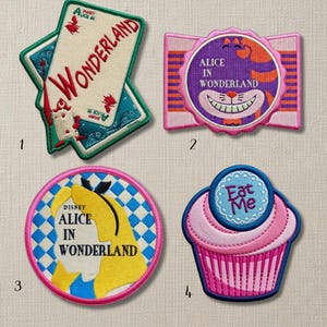 Op de afbeelding: Geborduurde patches met Alice in Wonderland-thema's. Ontwerpen omvatten een speelkaart, de Cheshire Cat, Alice's silhouet en een cupcake met de tekst "Eat Me". Elke patch heeft een unieke vorm en kleurenschema.