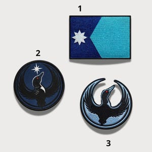 Peut inclure: Trois écussons brodés avec des motifs d'oiseaux et d'étoiles. L'un est rectangulaire avec un motif de drapeau bleu et turquoise et une étoile blanche. Les deux autres sont circulaires avec un motif d'oiseau et d'étoile.