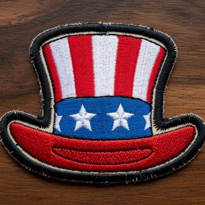 May include: Embroidered patch featuring a patriotic Uncle Sam hat design. The hat has red and white stripes, a blue band with white stars, and a red brim. The patch is outlined in black.