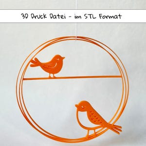 Könnte beinhalten: Orangene Vogeldekoration aus Metall. Zwei Vögel sitzen auf einem kreisförmigen Rahmen. Der Text "3D Druck Datei - im STL Format" steht oben. Die Vögel haben detaillierte Flügel und sind vor weißem Hintergrund.