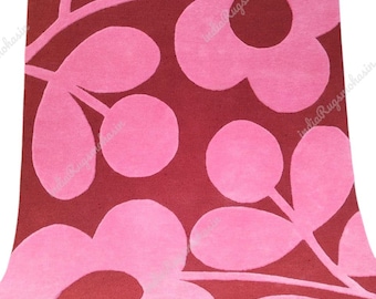 May include: A rectangular rug featuring a deep maroon background with a large-scale, repeating pattern of stylized pink flowers and rounded leaves. The design is rendered in a solid, flat color palette with clean, bold shapes across the surface.