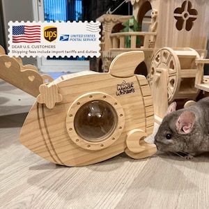 May include: A wooden submarine-shaped pet house with a porthole window and the text "Woodle Whiskers". The house is made of light-coloured wood and has decorative details. A small animal is near the house.