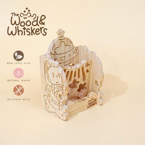 Pode incluir: Um organizador de mesa de madeira clara com um design de desenho animado. O organizador apresenta um design esculpido de um personagem semelhante a um gato e um topo decorativo. O texto "The Wood & Whiskers" é visível. Feito com cola não tóxica, madeira natural e sem pregos.